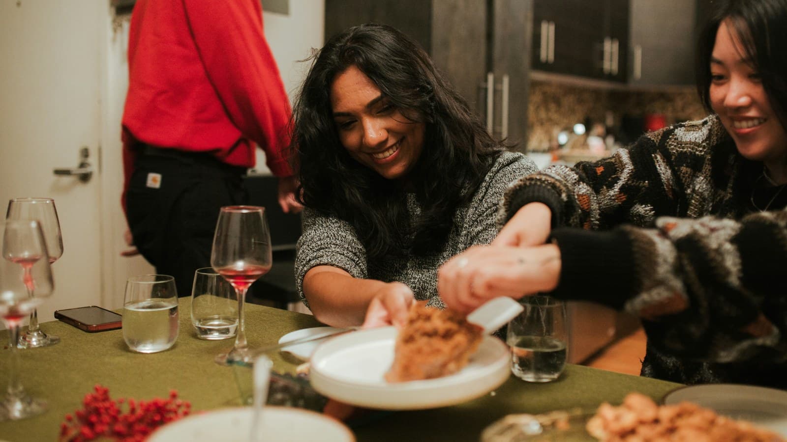 Friends sharing a meal around a table, one smiling as she serves a dish