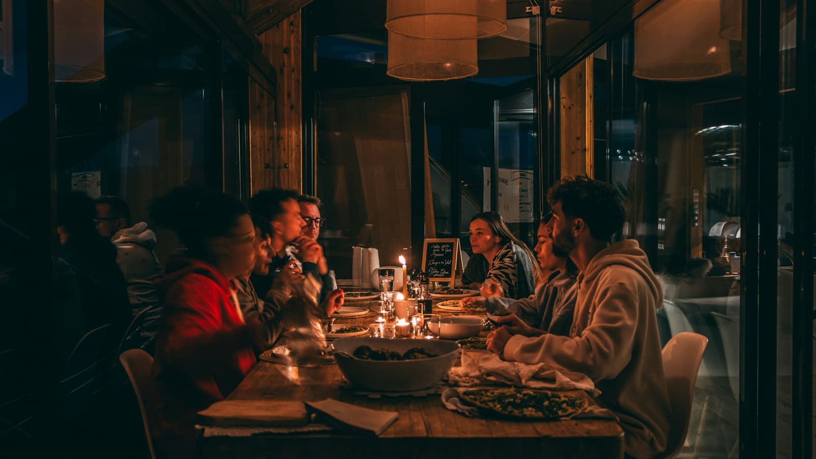 A group of people sharing a candlelit dinner around a long wooden table at night